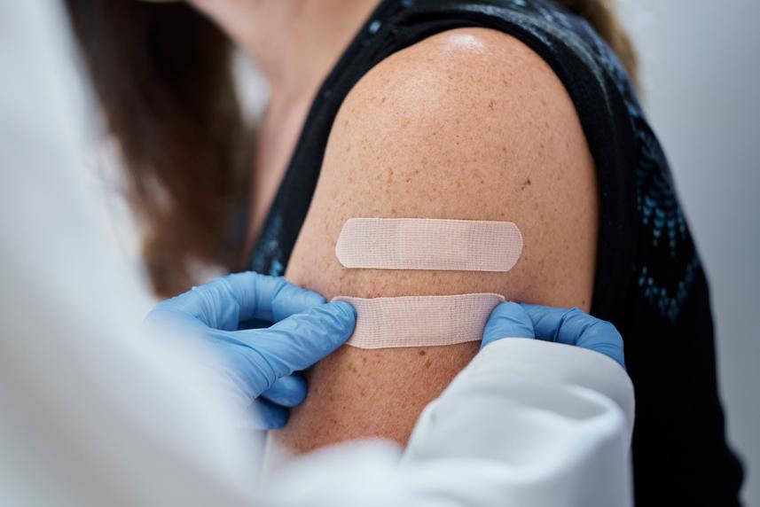 A doctor uses gloved hands to put a bandaid on a woman's arm.